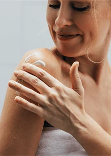 En kvinna smörjer in sin axel med lotion