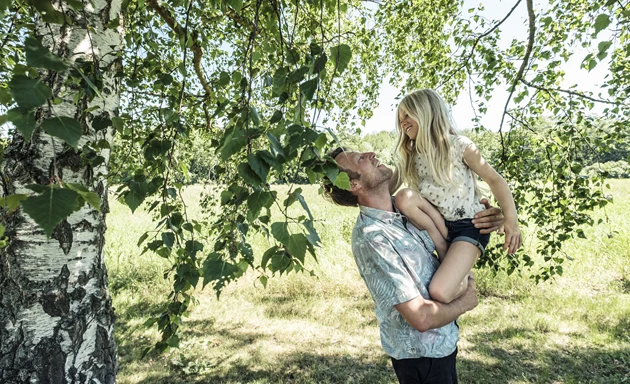 Pappa som bär sin dotter i famnen vid en björk under pollensäsongen.