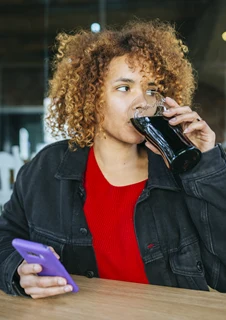 Kvinna dricker coca cola som innehåller socker som kan leda till hål i tänderna.
